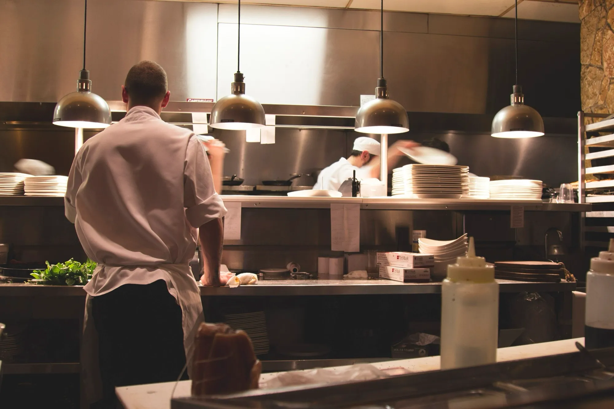 Cocinero de espaldas en el pase de una cocina profesional durante el servicio