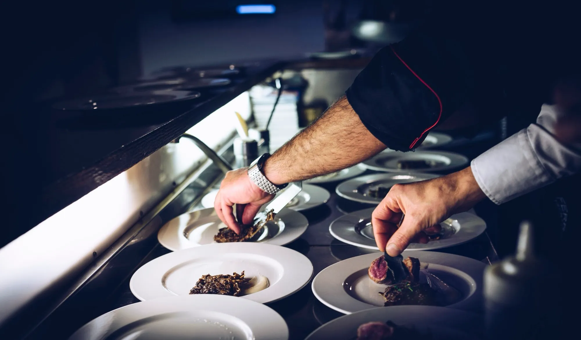 Manos de un cocinero emplatando una fila de platos